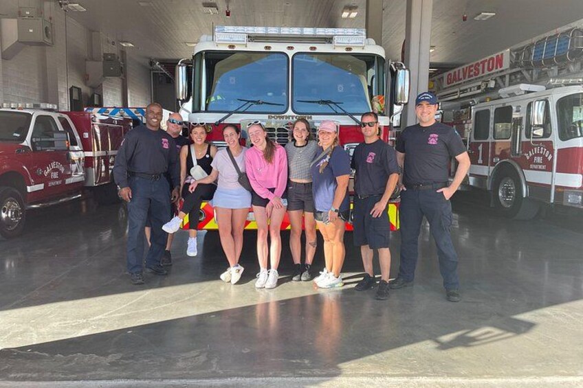 Un grupo de personas posando frente a un camión de bomberos en una estación de bomberos. 4