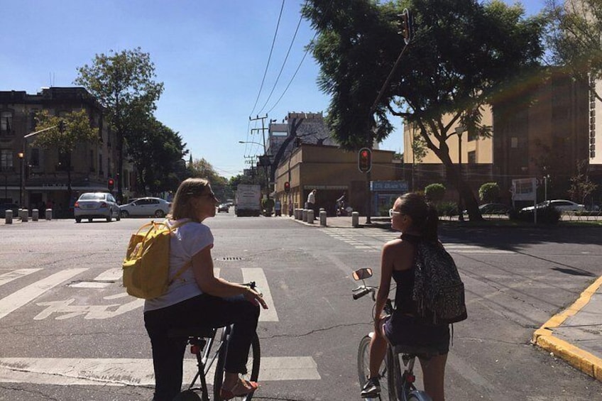 Två personer på cyklar vid ett övergångsställe med trafikljus och byggnader i bakgrunden. 4
