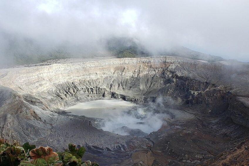 A volcanic crater with a central pool, surrounded by rugged terrain and mist. 1