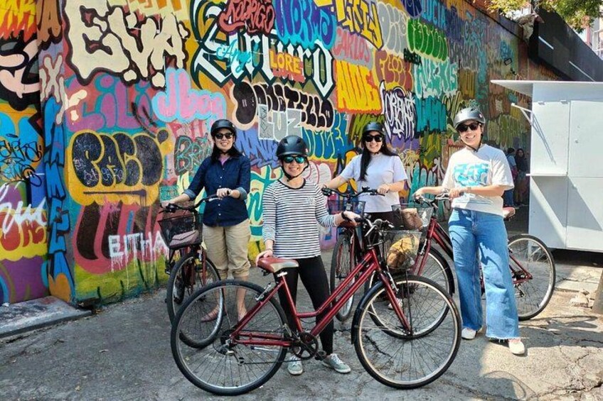 Een groep mensen met fietsen voor een kleurrijke muur met graffiti. 2