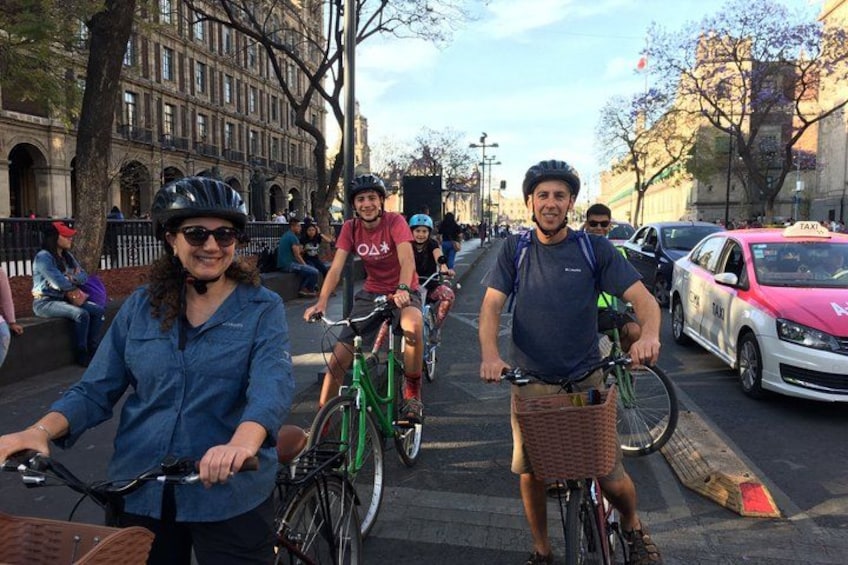 Des personnes à vélo circulent dans une rue de la ville, avec des immeubles et un taxi en arrière-plan. 3