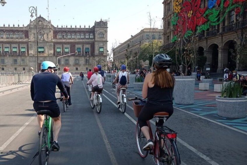 Des cyclistes sur une route asphaltée, avec des bâtiments et une grande sculpture florale en arrière-plan. 4