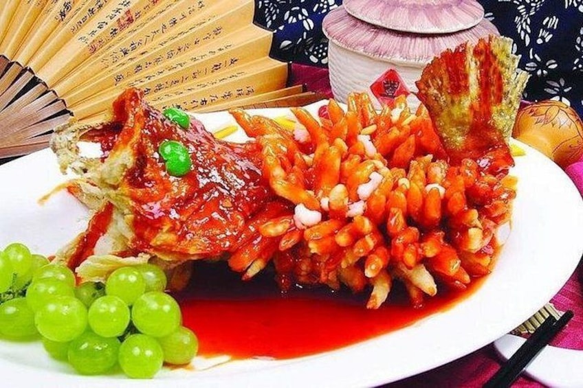 A whole cooked fish with a red sauce, garnished with green grapes and onions, on a white plate. 5