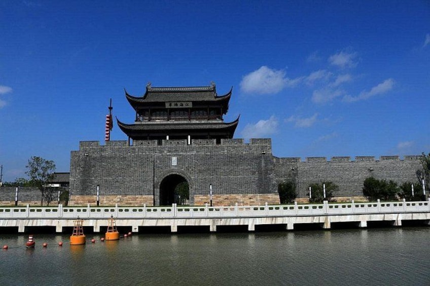 A traditional Chinese building with a tiled roof and a large archway, situated by a calm body of water with a bridge in the foreground. 3