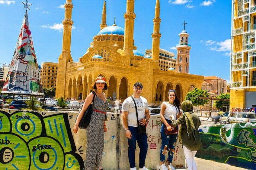 A mosque with multiple minarets, a large dome, and a minaret with a star on top. There is graffiti on a wall in the foreground. 5