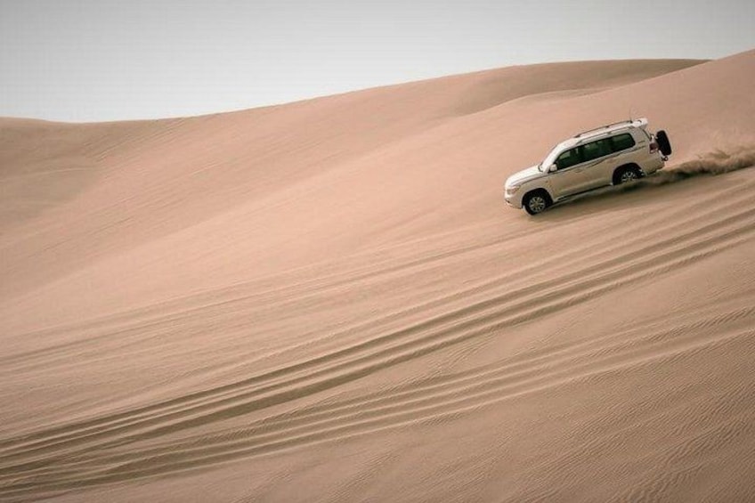 Een witte SUV rijdt door een woestijn met zandduinen. 2