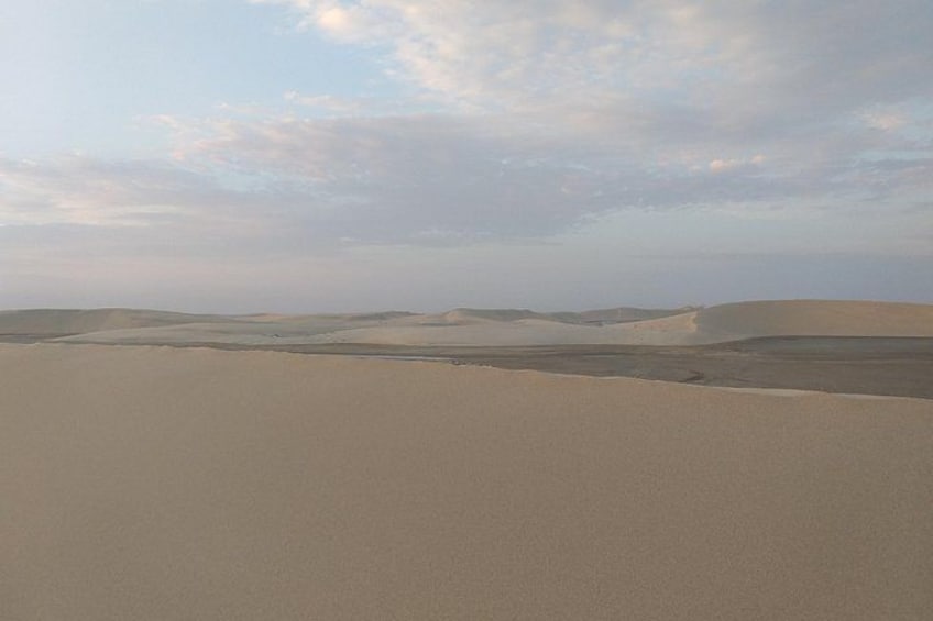 Een woestijnlandschap met zandduinen en een bewolkte lucht. 3