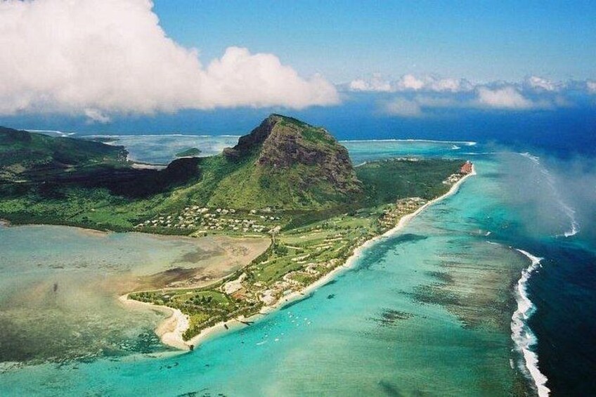 An aerial view of a coastal area with a prominent mountain, clear turquoise waters, and a small settlement. 2