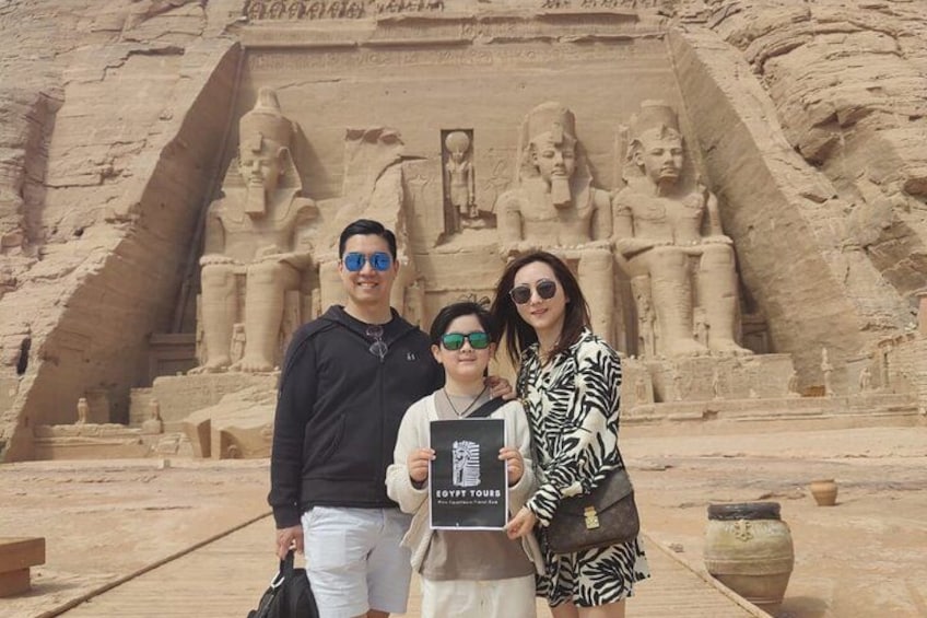 A group of people in front of a large ancient Egyptian monument with hieroglyphs and statues. 1