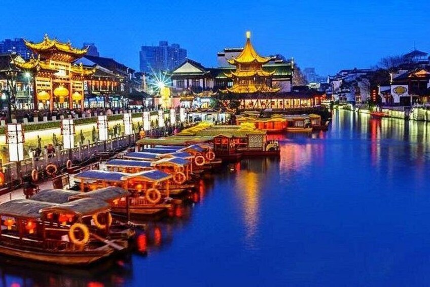 A river with traditional boats, illuminated buildings, and a bridge. 1