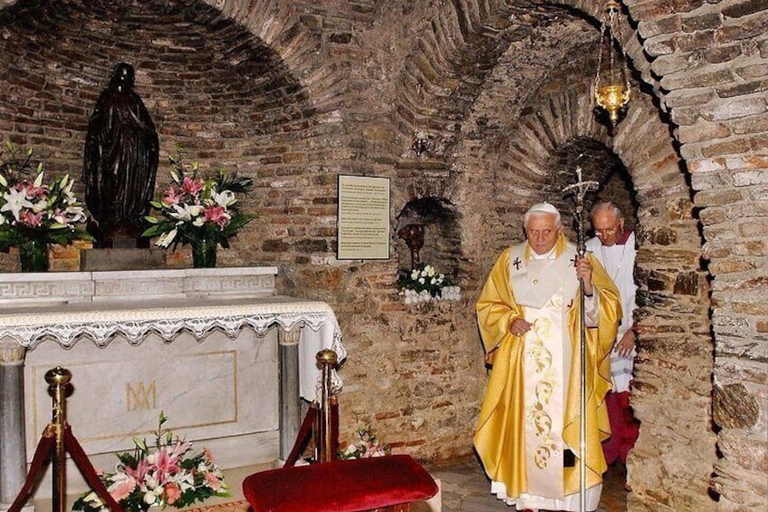 A religious figure in a stone-walled room with a statue, altar, and flowers. 5