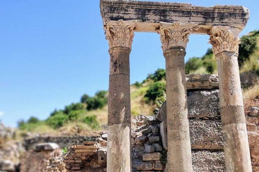 Ancient stone columns with intricate carvings, set against a backdrop of a clear sky and a hilly landscape. 3