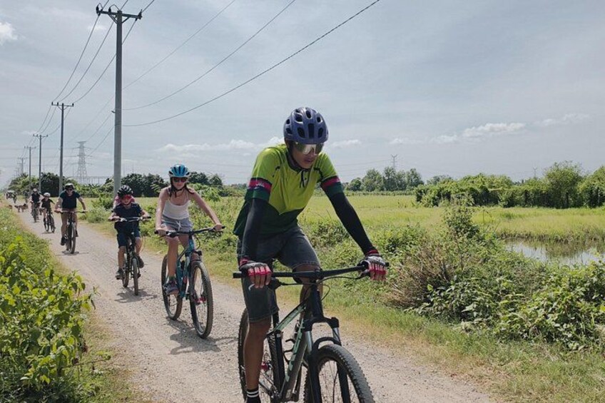 Cyclists on a rural road with greenery and power lines in the background. 1