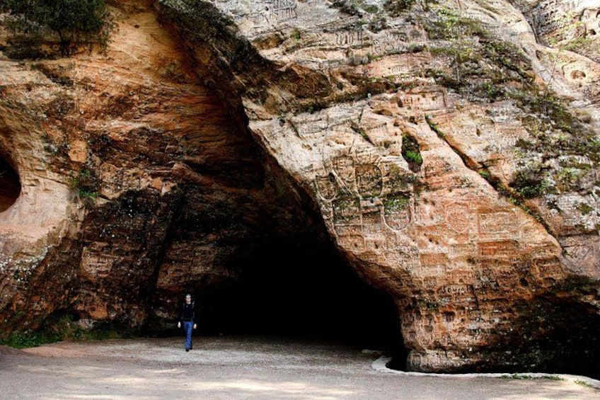 Una persona de pie frente a la entrada de una cueva con antiguos grabados en la roca. 2