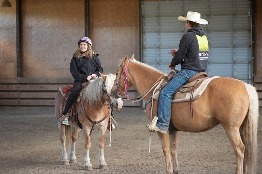 Two people on horses in an indoor arena with a building in the background. 4