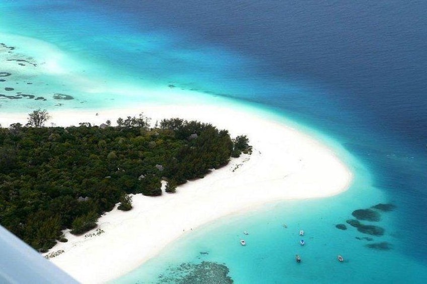 An aerial view of a white sandy beach with clear turquoise waters, surrounded by dense green vegetation. 1