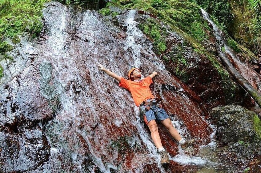A person climbing a waterfall in a forested area. 4