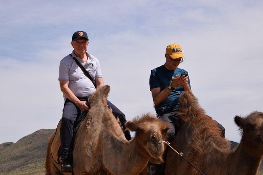 Two people riding camels in a desert landscape. 4