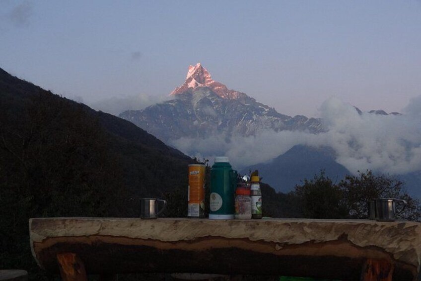 A mountain with a peak, surrounded by clouds, and a table with cans and a thermos in the foreground. 2