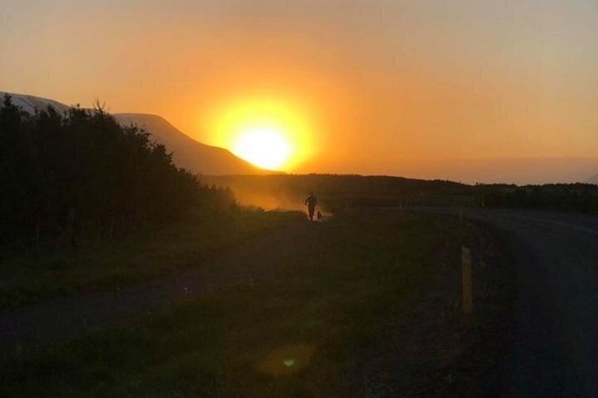 Solnedgang over et bakket landskab med en person, der går på en sti. 2