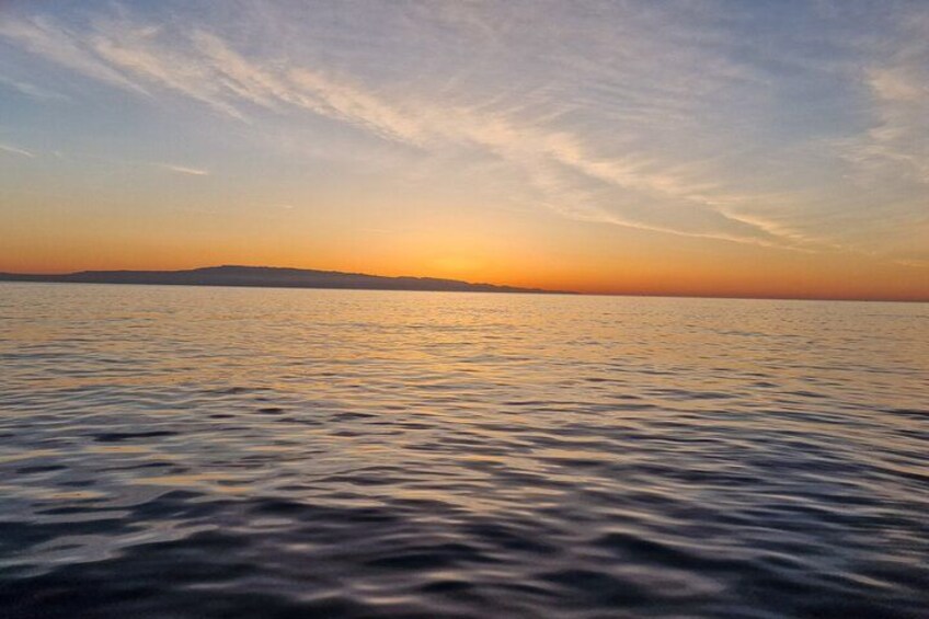 A calm sea at sunset with a distant landmass. 4