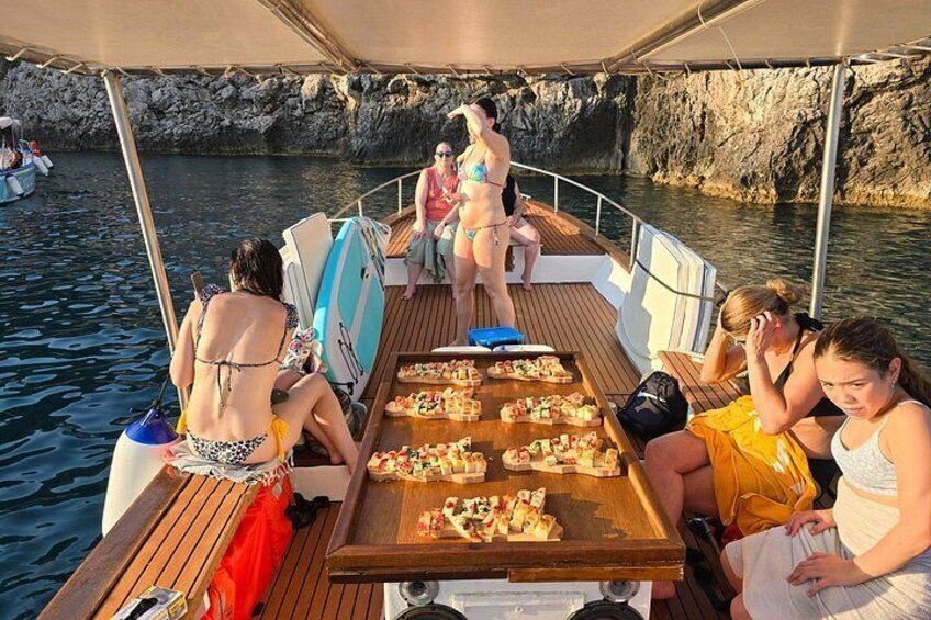 En båt med människor som sitter och står, ett bord med mat och klippiga branter i bakgrunden. 4