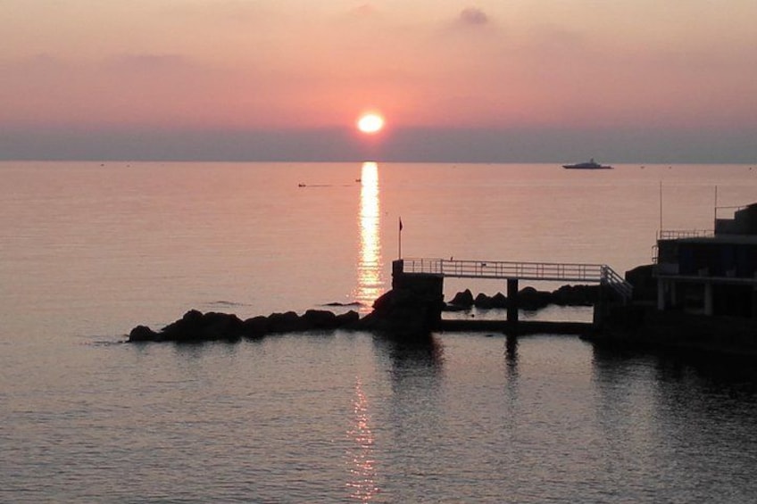 A sunset over a calm sea, a pier, and a distant boat. 4