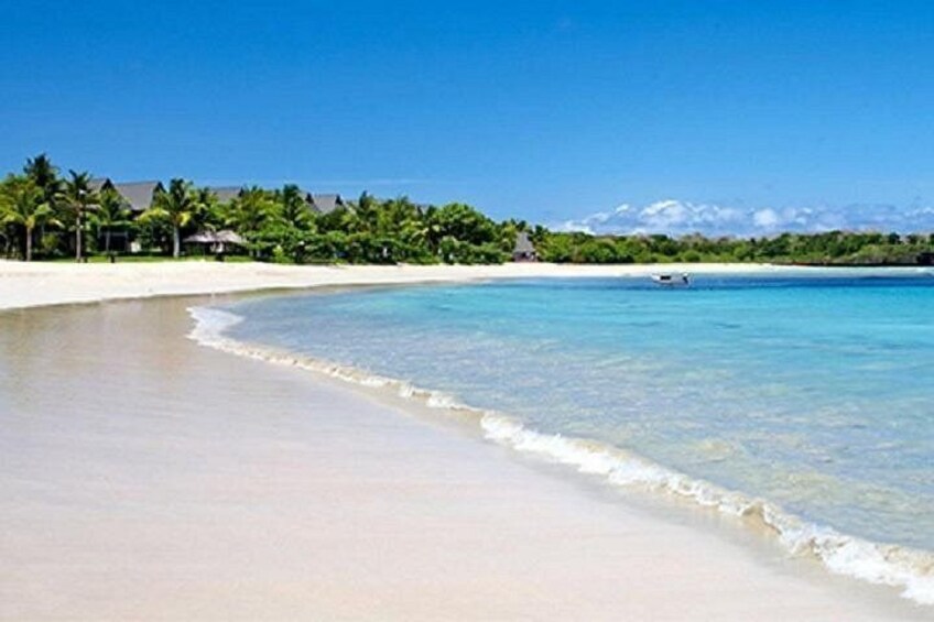 A beach with clear turquoise water, white sand, and a line of palm trees in the background. 1