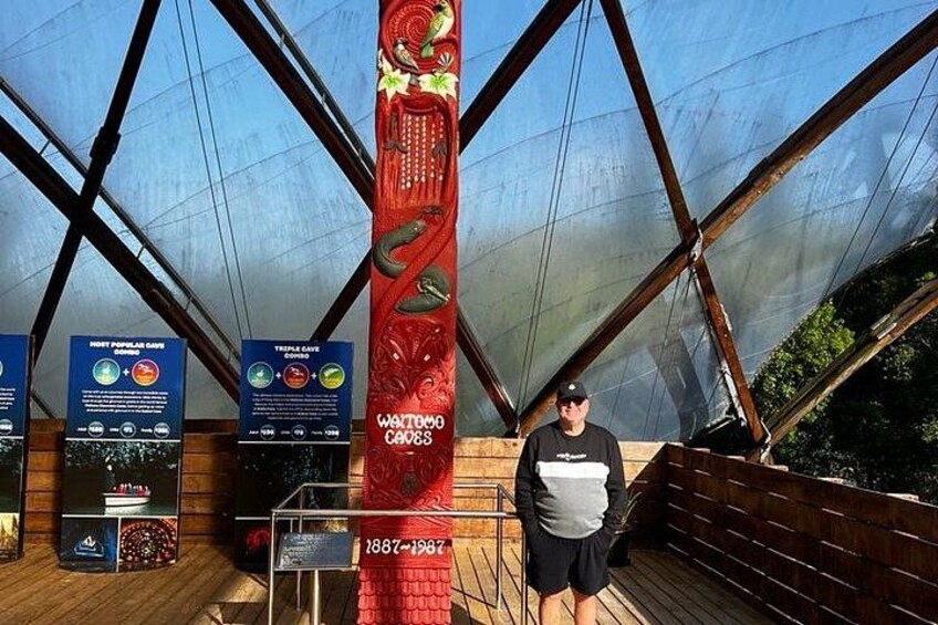 A person standing next to a red vertical display with text and graphics, in a structure with a glass roof and wooden beams. 2