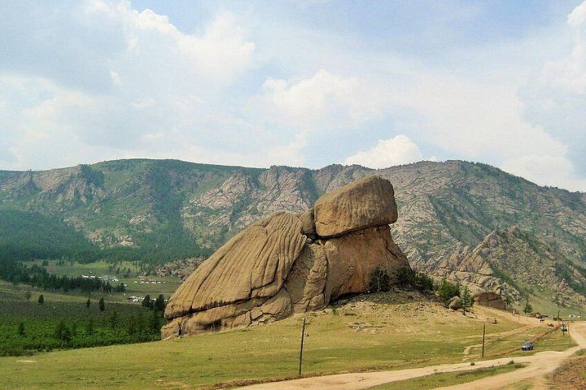 A large rock formation in a grassy field with a mountain in the background. 3