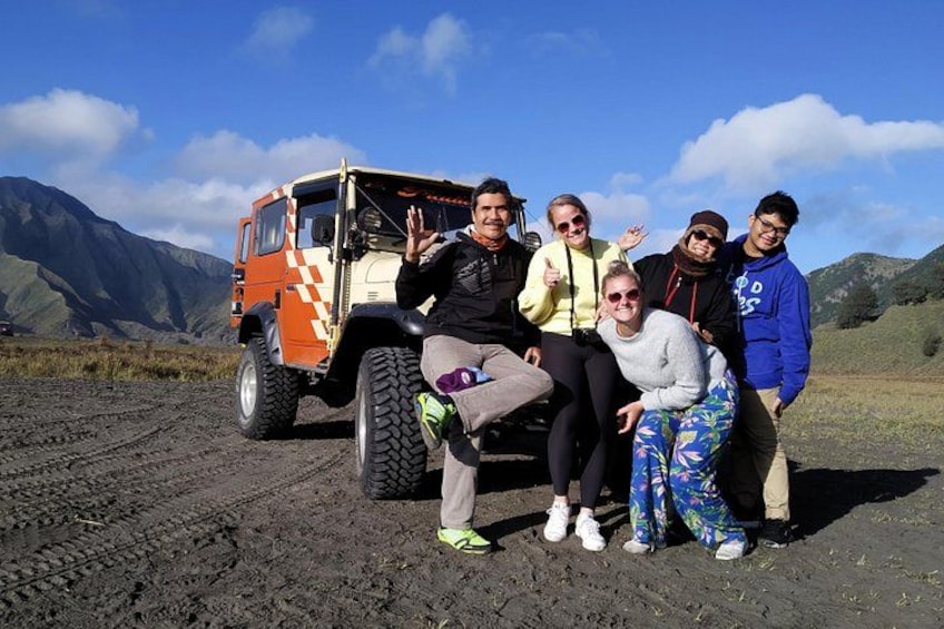 A group of people posing with a large off-road vehicle in a mountainous landscape. 3