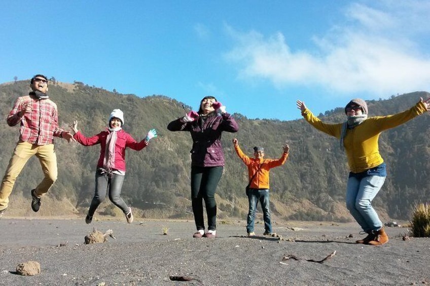 A group of people jumping on a rocky terrain with a mountainous background. 5