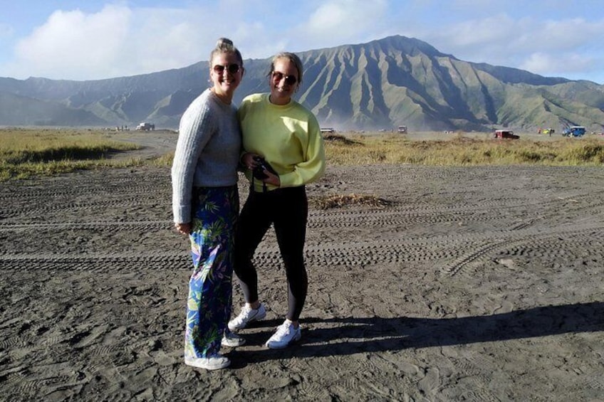Two people standing on a sandy terrain with a mountain in the background. 2