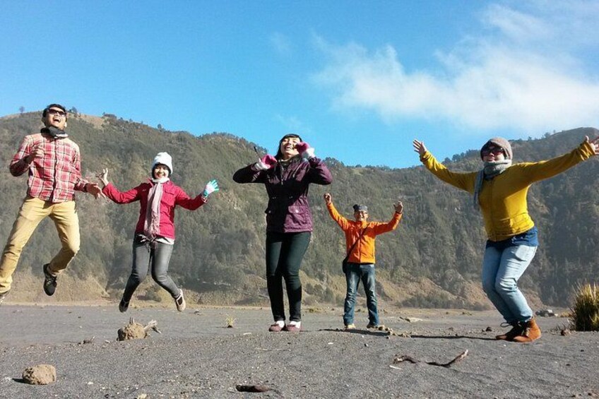 A group of people jumping on a rocky terrain with a mountainous background. 2