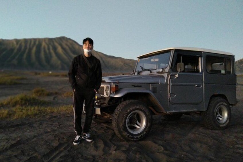 A person standing next to a dark-colored off-road vehicle in a desert landscape with mountains in the background. 4