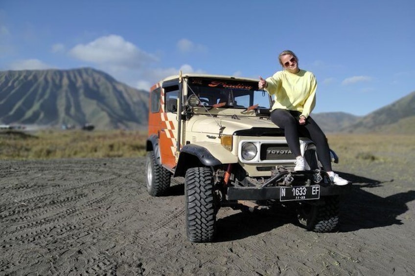 A person sitting on a Toyota off-road vehicle with a license plate on a dirt road with mountains in the background. 1