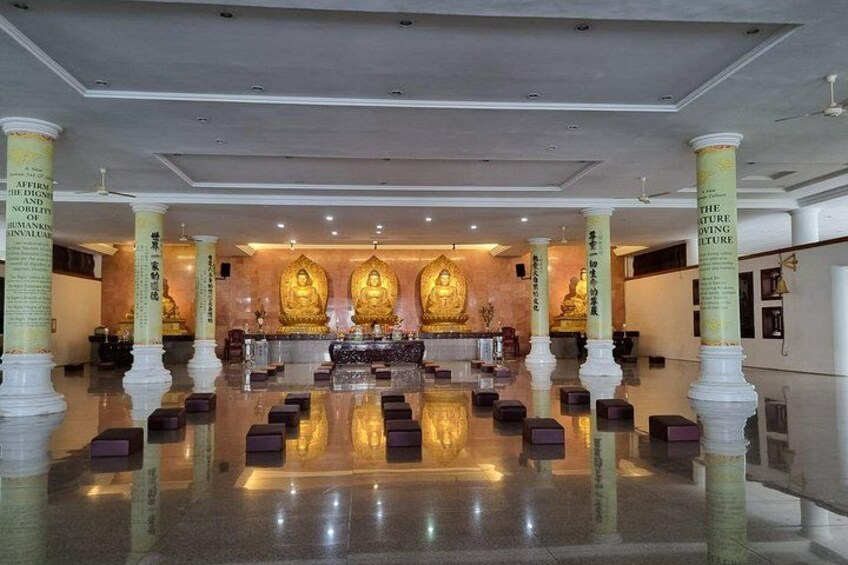 A spacious hall with golden Buddha statues, white pillars, and reflective flooring. 5