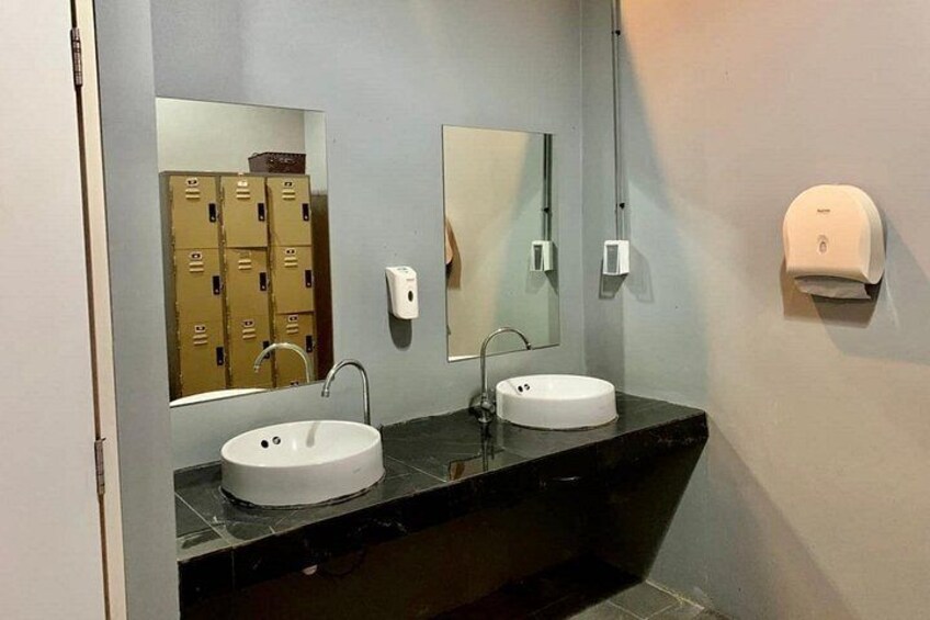 A restroom with two sinks, a mirror, a soap dispenser, and a storage area with lockers. 1
