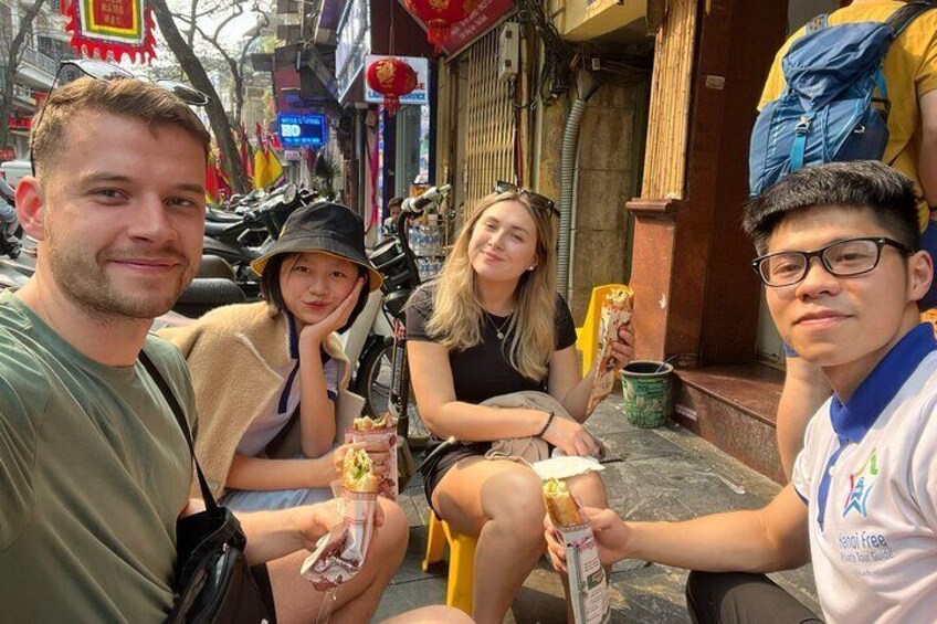 Four people sitting on a bench in a street with shops and motorcycles in the background. 2