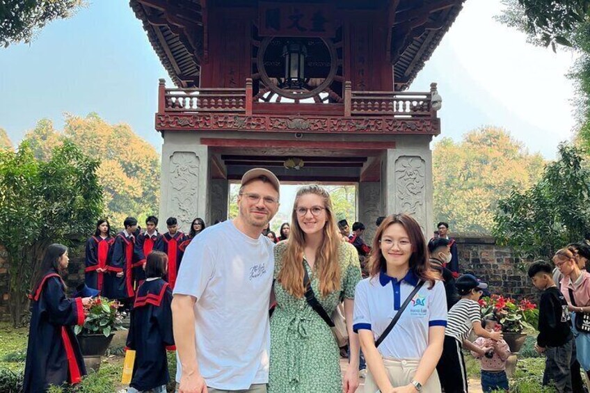 A group of people in traditional attire standing in front of a wooden pavilion with intricate carvings. 3