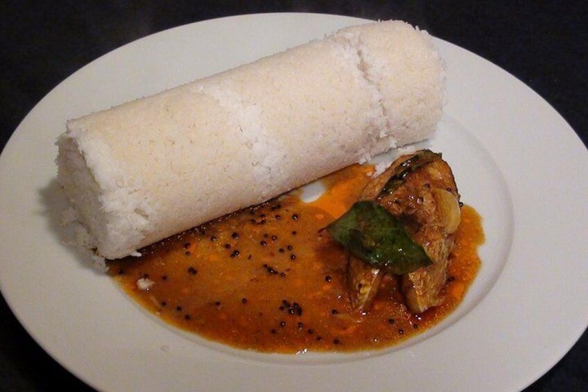 A white plate with a rolled white food item, possibly a dumpling, and a piece of meat in a reddish sauce. 2