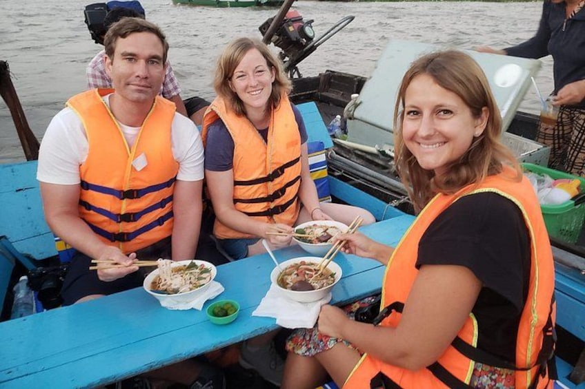 Drie mensen in een boot, met reddingsvesten, eten noedels. 5
