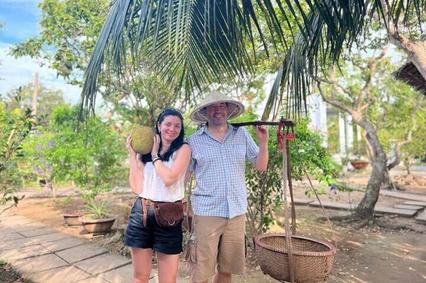 Two people holding a fruit and a tool in a garden. 1