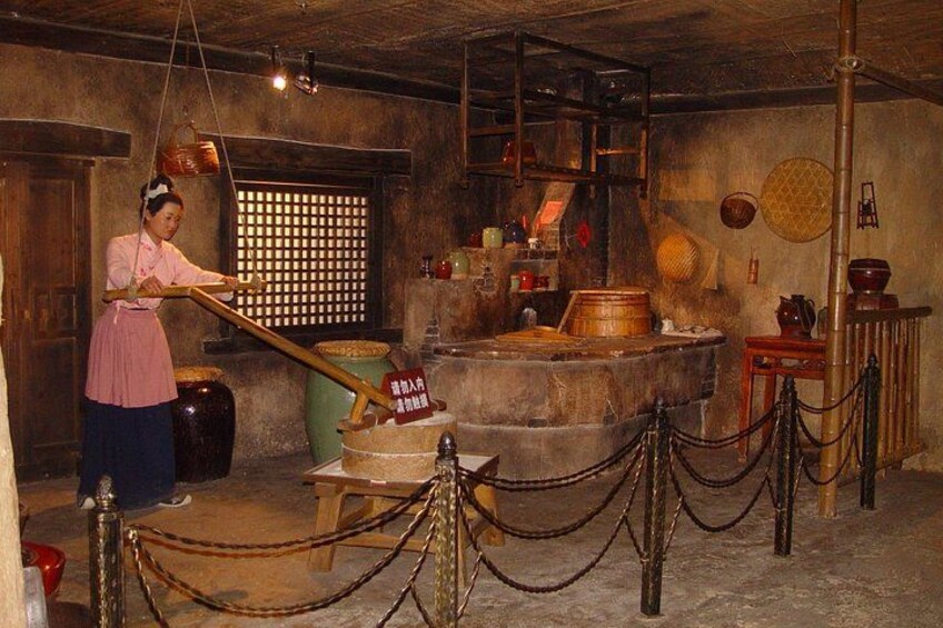 Une cuisine d’époque où l’on voit une femme utiliser un ustensile en bois, de grands pots et des ustensiles de cuisine traditionnels. 3