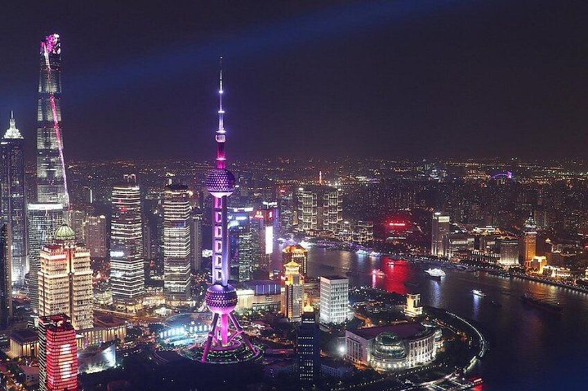 Une vue nocturne d’une ville, avec des gratte-ciel illuminés et une tour imposante surmontée d’une structure sphérique à sa base. 1