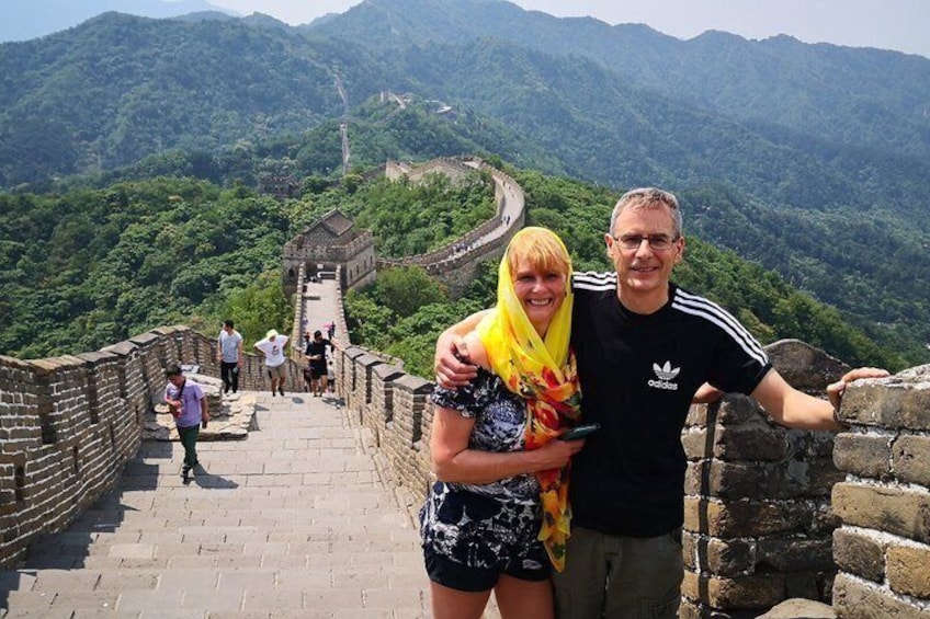 A couple on the Great Wall of China with lush green mountains in the background. 1
