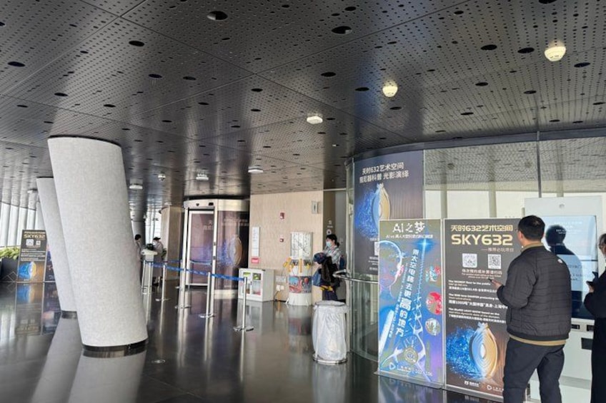 A modern indoor space with a large cylindrical column, a glass elevator, and informational posters. 2