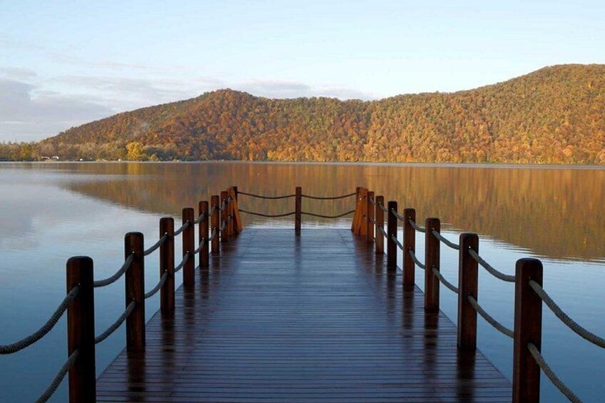 A wooden dock extending into calm water, surrounded by autumn-colored trees and hills. 1