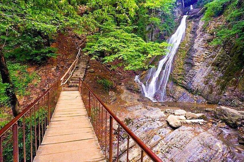 A wooden bridge with metal railings leading to a waterfall in a forested area. 5