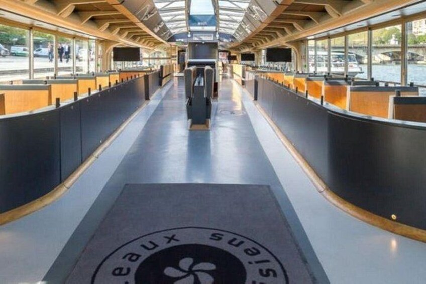 A modern train interior with a central aisle, seating on both sides, and a logo on the floor. 1